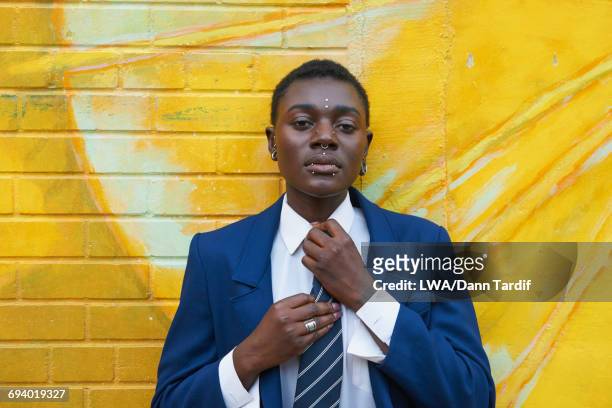 Androgynous Black woman leaning on mural adjusting tie