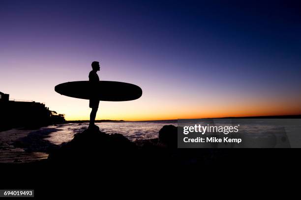 silhouette of hispanic man holding surfboard at beach - hot latin nights stock pictures, royalty-free photos & images