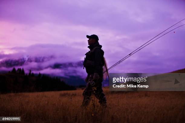 caucasian man walking and carrying fishing rods - fishing for leave stock-fotos und bilder