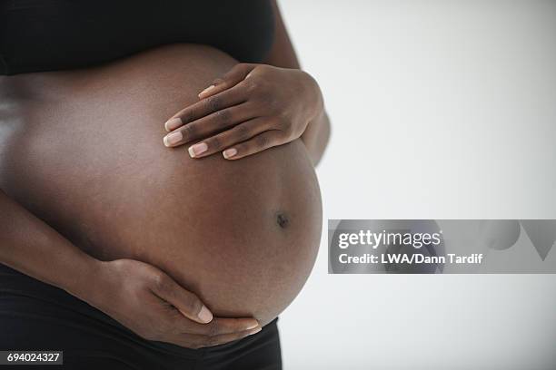 midsection of pregnant black woman holding belly - pregnant lady stock-fotos und bilder