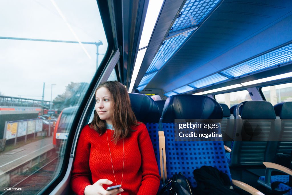 Young woman sitting in the train holding her smart phone looking into the window