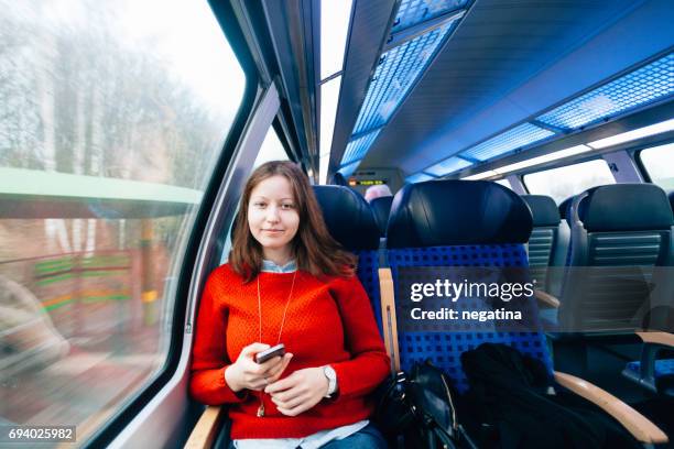 young woman sitting in the train holding her smart phone looking to the camera - die letzte reise photo call in hamburg stock-fotos und bilder