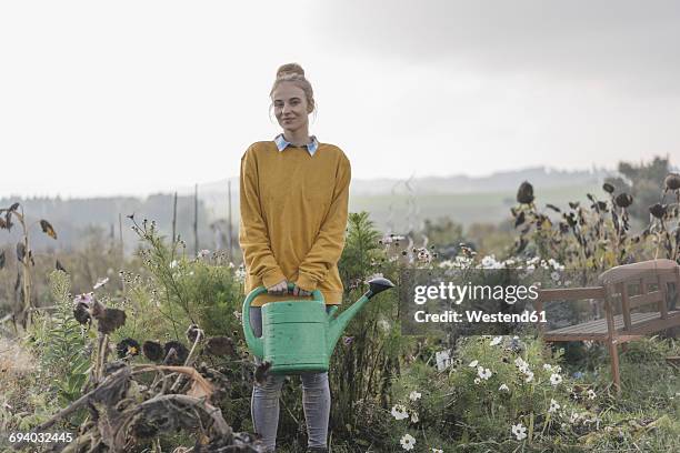 smiling young woman holding watering can in cottage garden - dead women stock-fotos und bilder