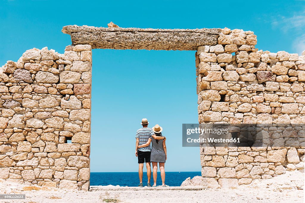 Greece, Milos, Firopotamos Beach, Couple standing in door in stone wall, looking at distance