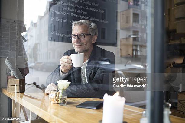 mature man drinking coffee in a cafe - café homme vitre photos et images de collection