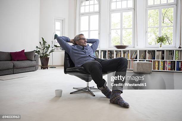 relaxed mature man at home sitting in chair - man middelbare leeftijd woonkamer stockfoto's en -beelden