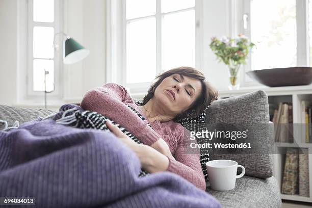 woman with stomach ache lying on the sofa - krankheit stock-fotos und bilder