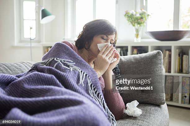 woman having a cold lying on the sofa - blowing nose stock pictures, royalty-free photos & images