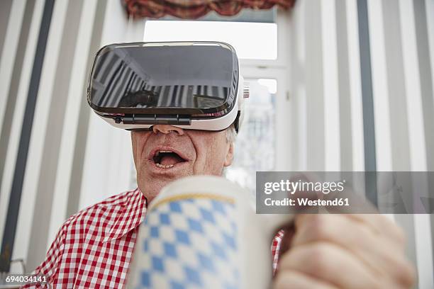 senior man holding beer mug wearing vr glasses - altbier stock-fotos und bilder