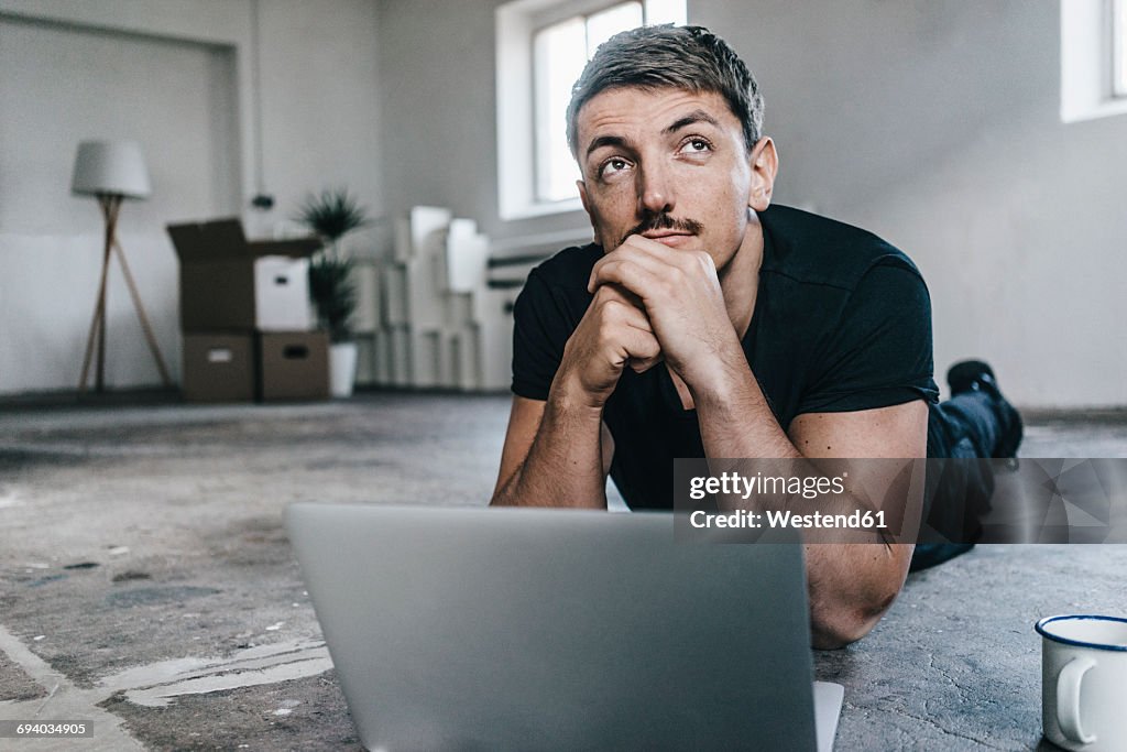 Man lying on floor with laptop in empty loft