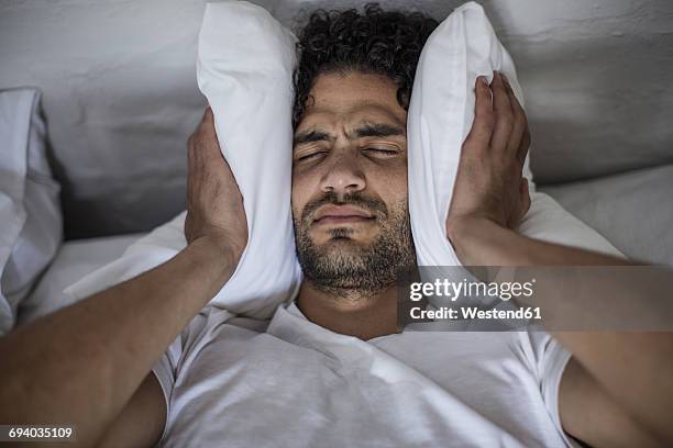 young man covering his ears with a pillow - inconvenience stock-fotos und bilder