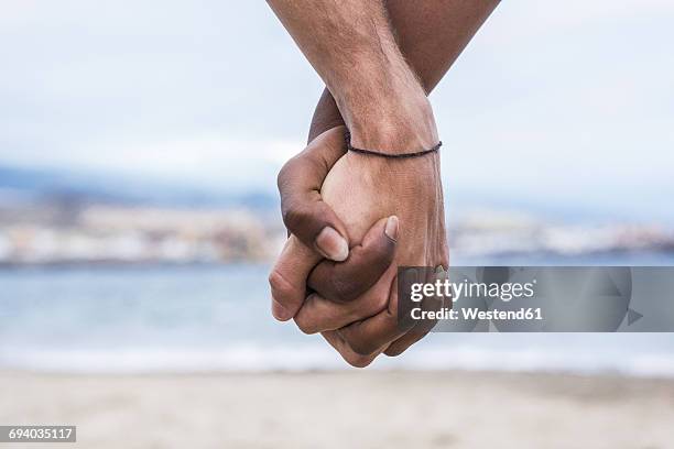 close-up of two hands connected on the beach - 2 guys black white stock-fotos und bilder