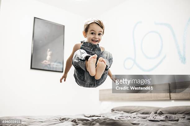 happy little boy jumping on the bed - a boy jumping on a bed fotografías e imágenes de stock