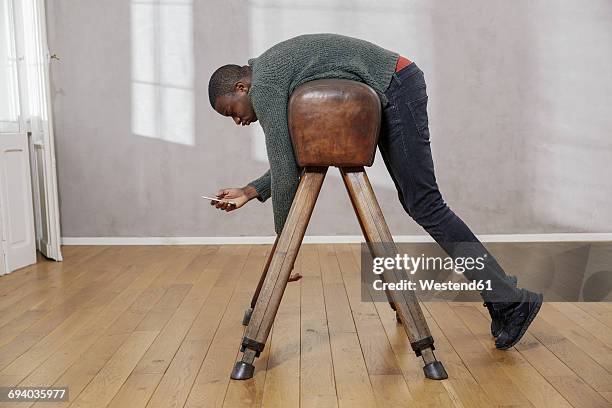 young man hanging out on pommel horse looking at smartphone - seulement des adultes photos et images de collection