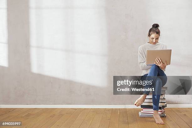 young woman sitting on stack of books using laptop at home - online reading stock pictures, royalty-free photos & images