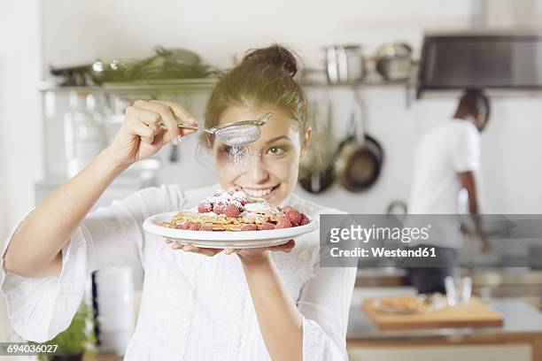 portrait of young woman sprinkling icing sugar on waffles in the kitchen - action cooking fotografías e imágenes de stock