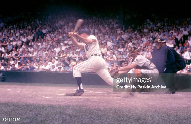 Harvey Kuenn of the Detroit Tigers swings at the pitch as catcher Gus Triandos of the Baltimore Orioles sets up behind home plate during an MLB game...