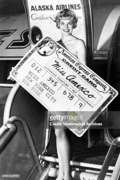 Portrait of the recently named Miss Amexco, Lynn Weston, as she poses, seemingly naked behind an oversized novelty American Express credit card,...