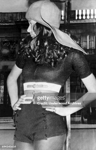 An unidentified model poses, hands on her hips, in an oversized felt sailor's cap and a large, corset-style belt over a semi-transparent knit,...