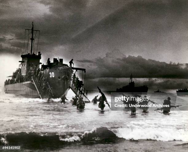 View of Allied troops from a transport vessel, among them medics with stretchers over their shoulders, as they wade ashore during the invasion of...