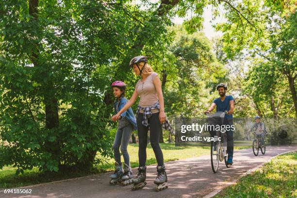 family roller skating and riding bicycle - adult riding bike through park stock pictures, royalty-free photos & images