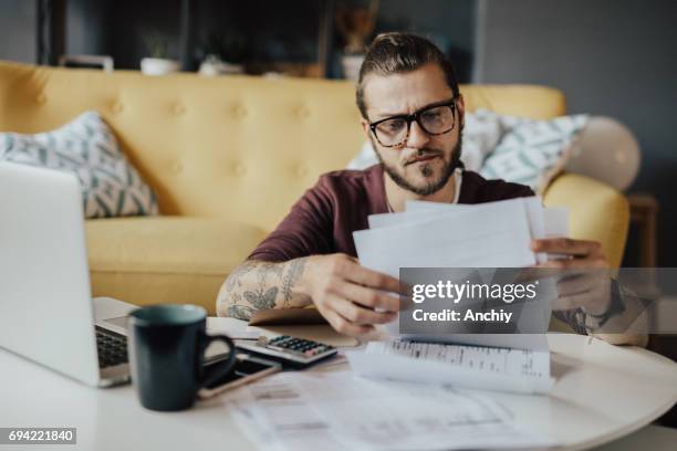 hombre joven maneja los gastos del hogar - calculadora fotografías e imágenes de stock