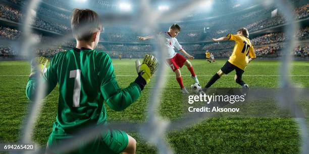 fútbol los niños a jugadores marcar un gol. el portero intenta golpear la bola - competición de fútbol fotografías e imágenes de stock