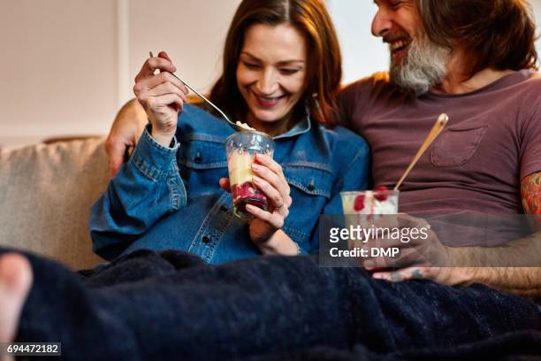 happy mature couple sitting on sofa and eating ice cream. - dessert stock pictures, royalty-free photos & images