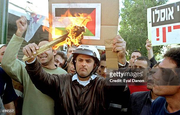 An angry Israeli burns a printed Palestinian flag at the sceneof a suicide bombing January 25, 2002 in Tel Aviv. The Palestinian bomber blew himself...