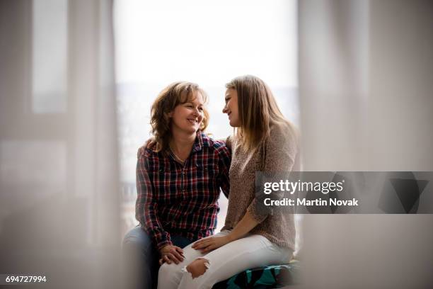 adult daughter and mother conversing at window - girl with mother stock-fotos und bilder