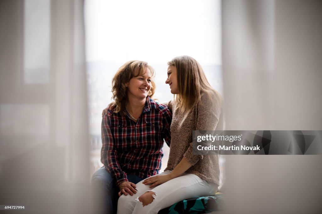 Adult daughter and mother conversing at window
