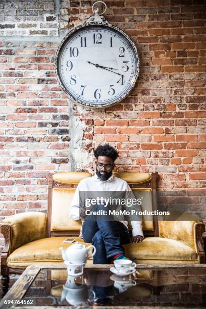 man sitting in teashop under large clock - tea room fotografías e imágenes de stock