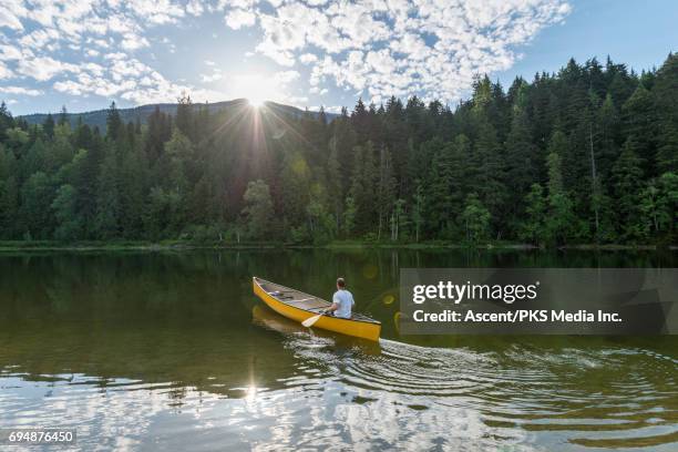 man paddles canoe across mountain lake, sunrise - rowing boat stock pictures, royalty-free photos & images