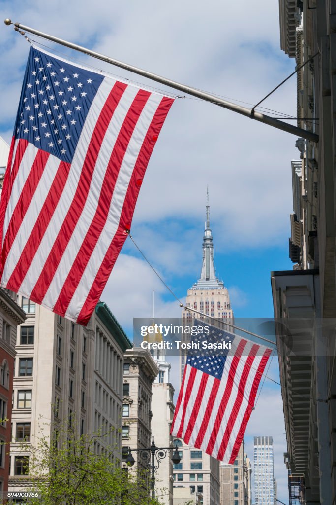 The American National Flags are hoisted among the Fifth Avenue in New York City. Empire State Building can be seen behind in the clouds.