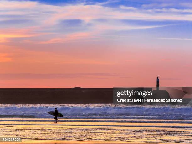 the silhouette of a surfer and a small lighthouse with the last lights of the sunset. - cantabria stock pictures, royalty-free photos & images