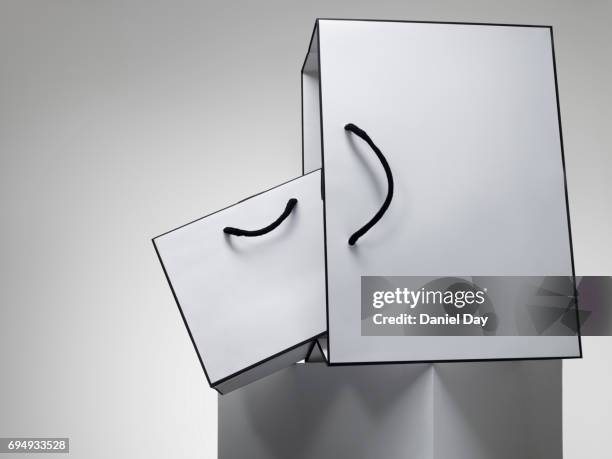 a series of white shopping bags stacked on a white plinth against a grey background - sac blanc photos et images de collection