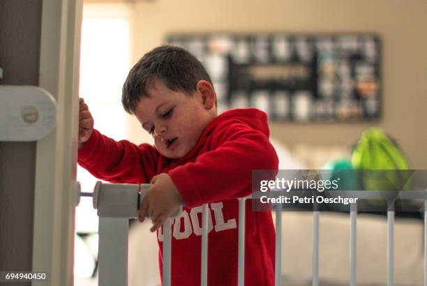 a young boy tries to open a child security gate. - baby gate stock pictures, royalty-free photos & images