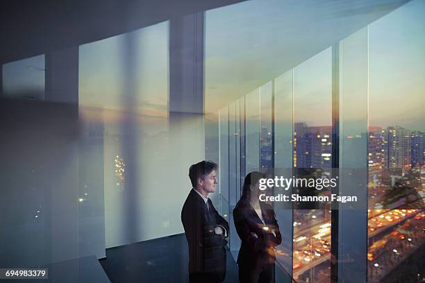 business colleagues looking out window in office - woman looking out window with city lights stock pictures, royalty-free photos & images