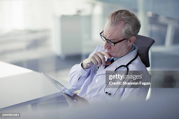 doctor looking at tablet computer in office - la care health plan stock-fotos und bilder