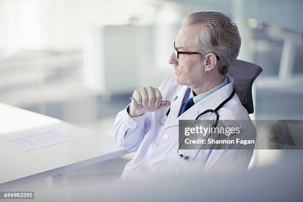 doctor sitting in office looking forward - forward thinking stock-fotos und bilder