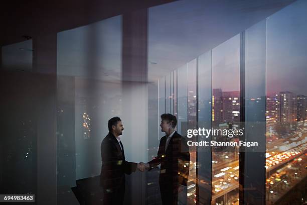 businessmen shaking hands in office at night - partnership fotografías e imágenes de stock