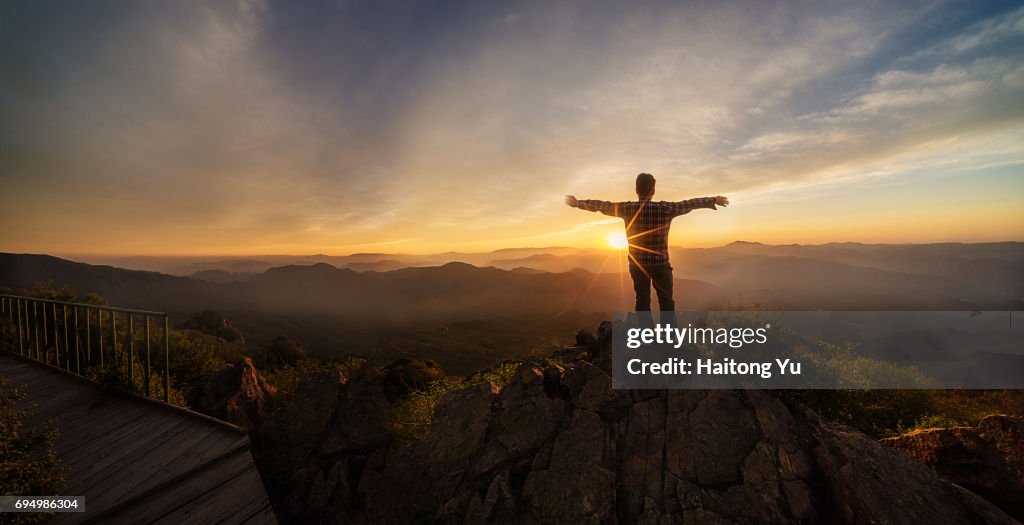Man facing sunset with arm stretched