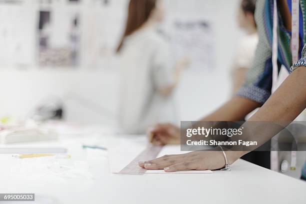 woman measuring fabric in fashion design studio - sastre fotografías e imágenes de stock