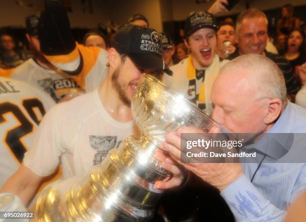 Captain Sidney Crosby of the Pittsburgh Penguins helps general manager Jim Rutherford with a drink from the Stanley Cup in the locker room after Game...