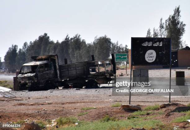 General view shows a burnt out vehicle next to a banner bearing the Islamic State group's flag in the village of Dibsiafnan on the western outskirts...