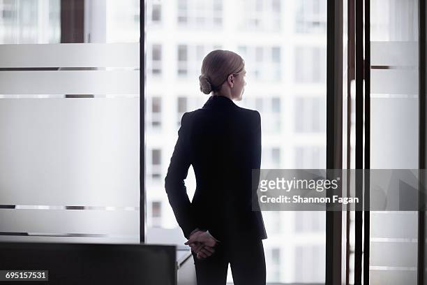 businesswoman standing looking out office window - three quarter length stockfoto's en -beelden