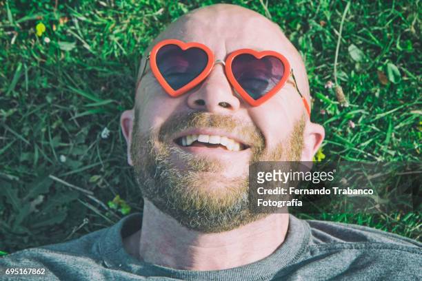 man lying on the grass with red heart shaped sunglasses - verliefd worden stockfoto's en -beelden