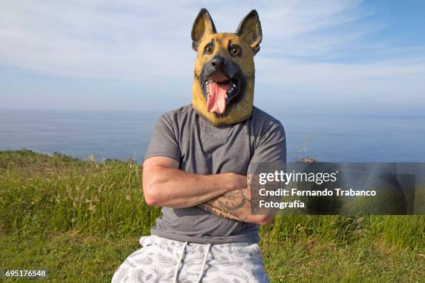 man with tattooed arm and german shepherd dog mask with arms crossed by the sea - german shepherd bark stock pictures, royalty-free photos & images