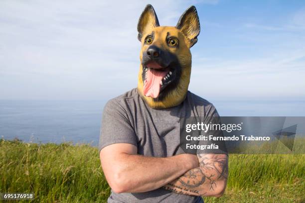 man with tattooed arm and german shepherd dog mask with arms crossed by the sea - german shepherd face stock pictures, royalty-free photos & images