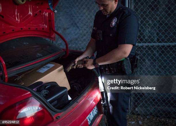 Police officer checks an air pistol found in the trunk of a car while other police question several Crip gang members May 21, 2017 for a violation of...